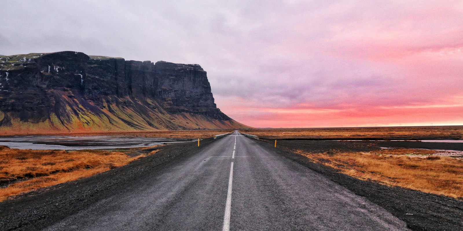 An empty road at sunset running toward a flat-topped mountain in Iceland